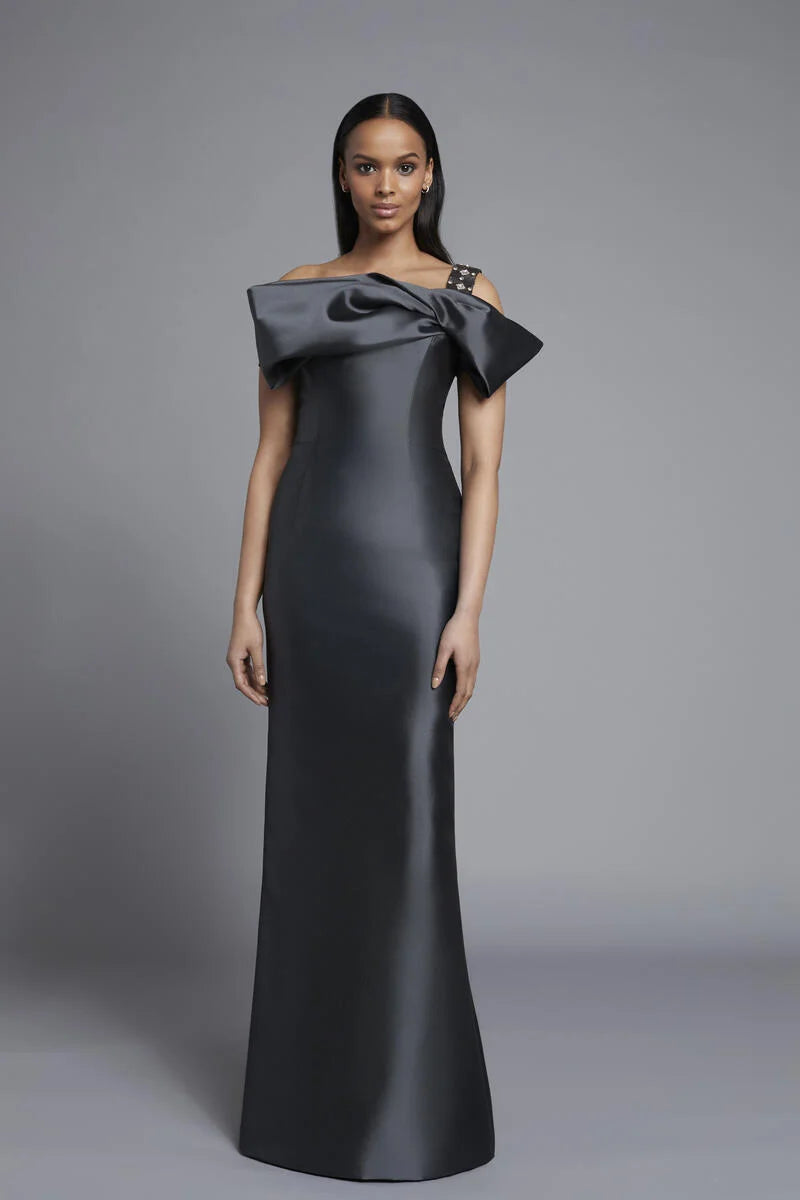 A woman modeling a floor-length off-the-shoulder gown in grey against a neutral gray studio background.