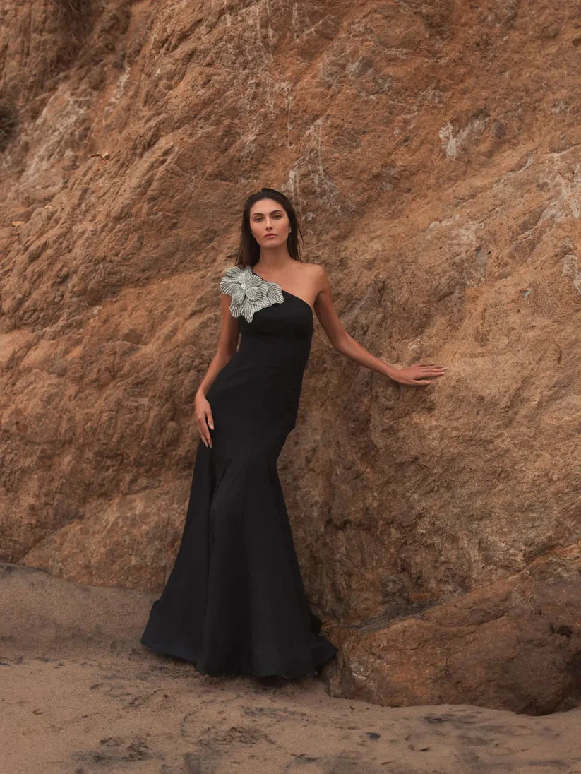 Model wearing Mac Duggal 11810 one-shoulder trumpet gown with flower detail, posing outdoors.