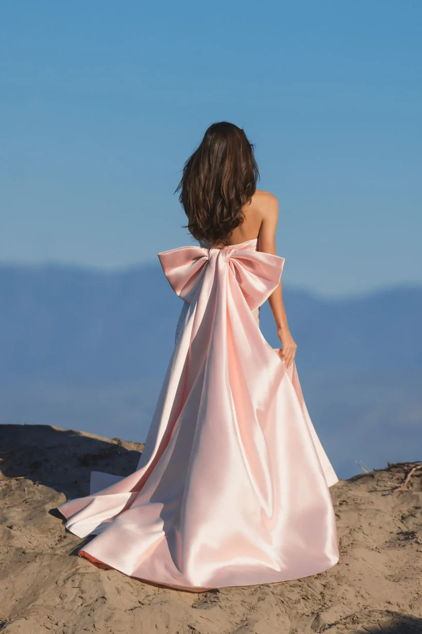 Model wearing Mac Duggal 37011 strapless gown featuring a sleek silhouette with an oversized bow detail on the back. Back view. Model wearing the color blush.