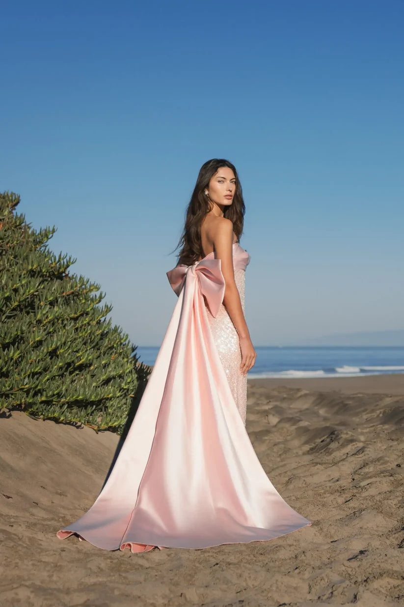 Model wearing Mac Duggal 37011 strapless gown featuring a sleek silhouette with an oversized bow detail on the back. Back 3/4 view. Model wearing the color blush.