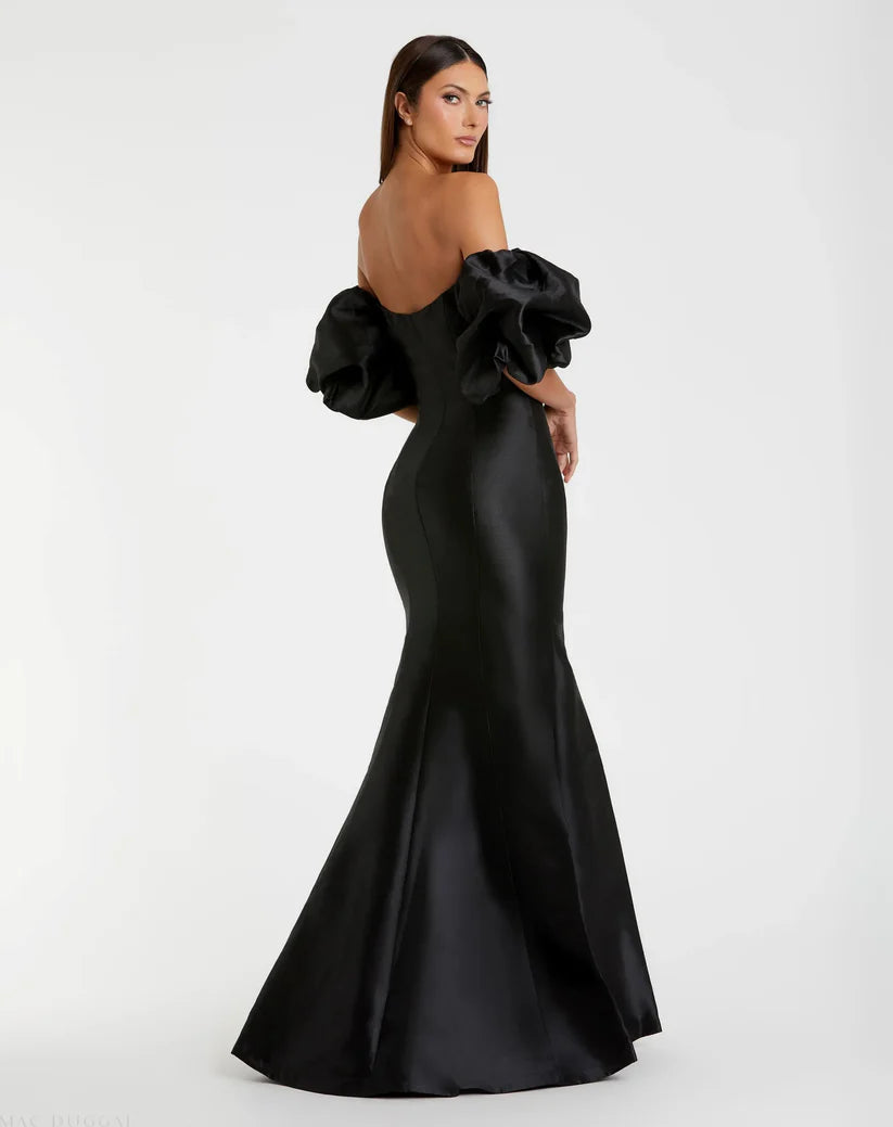 Model wearing Mac Duggal 50677 off-the-shoulder satin gown with puff sleeves, mermaid silhouette, and sweeping train. Model is wearing the color black. Back view.