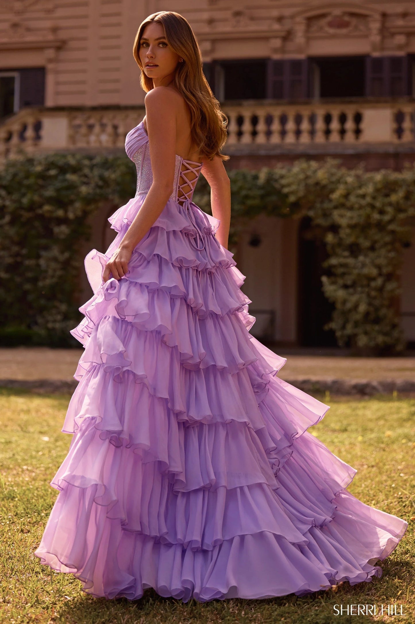 Model wearing Sherri Hill 57288 gown with strapless hot fix corset and layered ruffle slit skirt