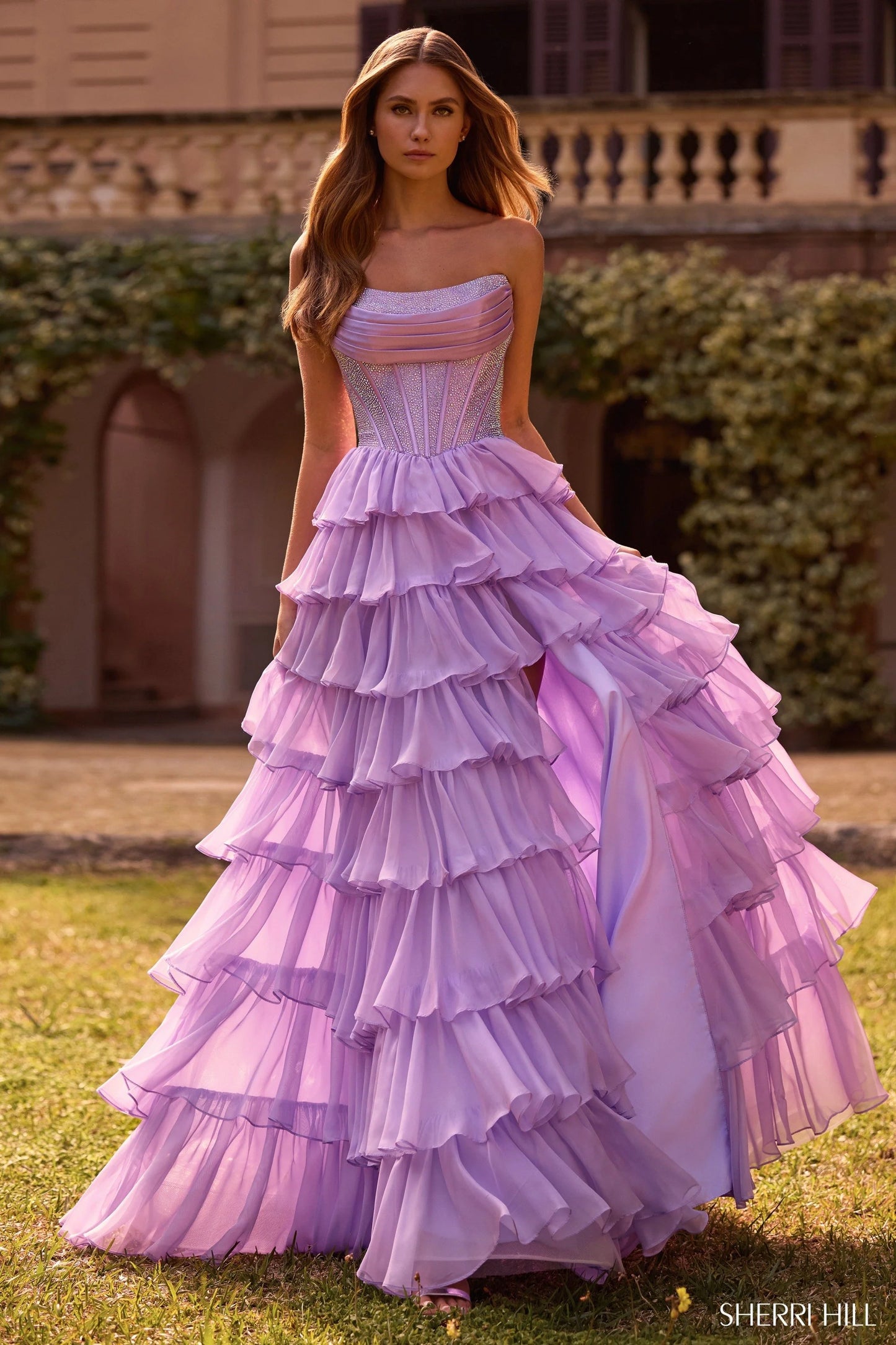 Model wearing Sherri Hill 57288 gown with strapless hot fix corset and layered ruffle slit skirt
