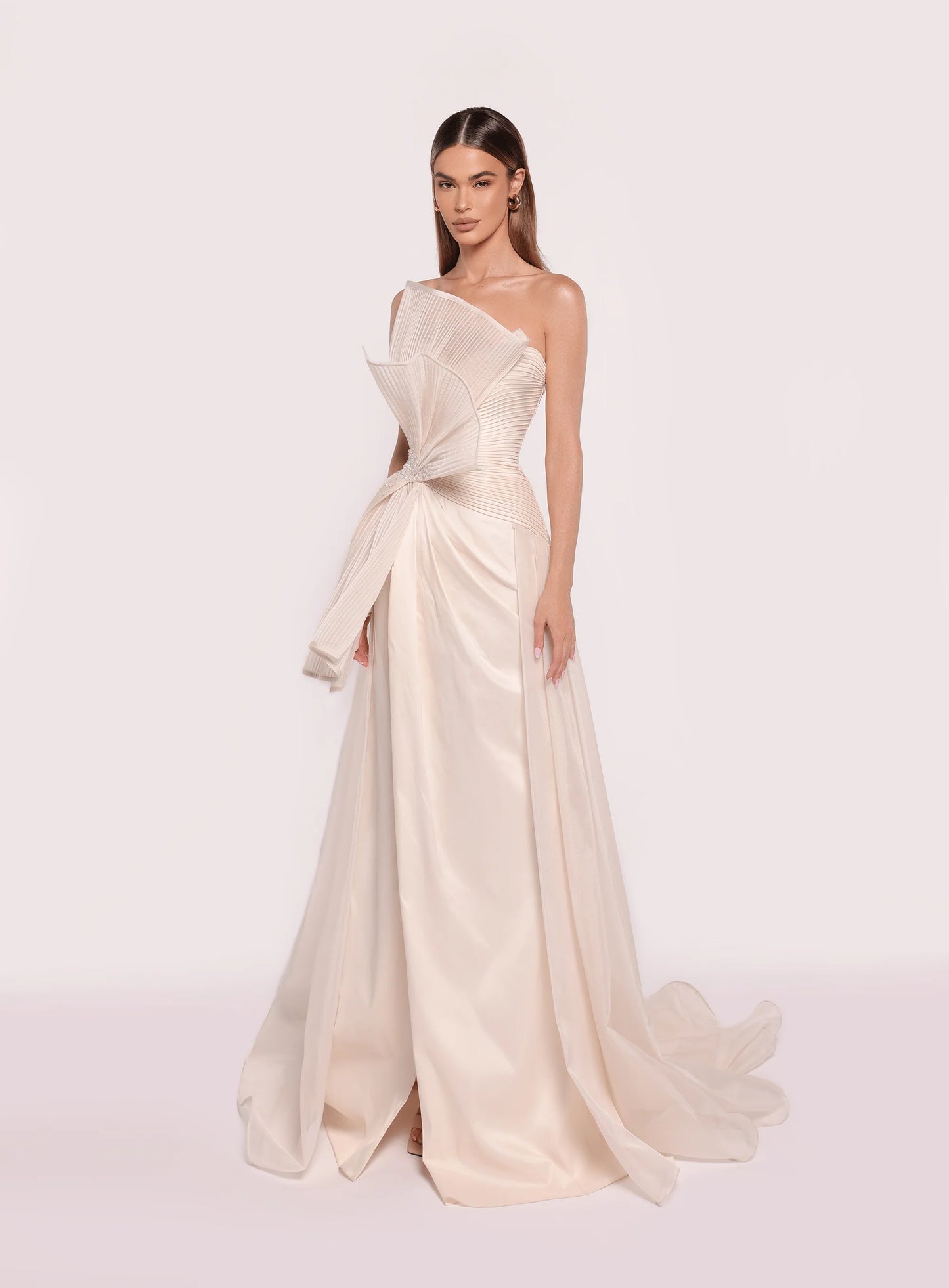 Model wearing Tarik Ediz 98708 Ronesme strapless gown in the color vanilla with sculptural pleated bodice and full A-line skirt with train, ideal for red carpet or formal events.