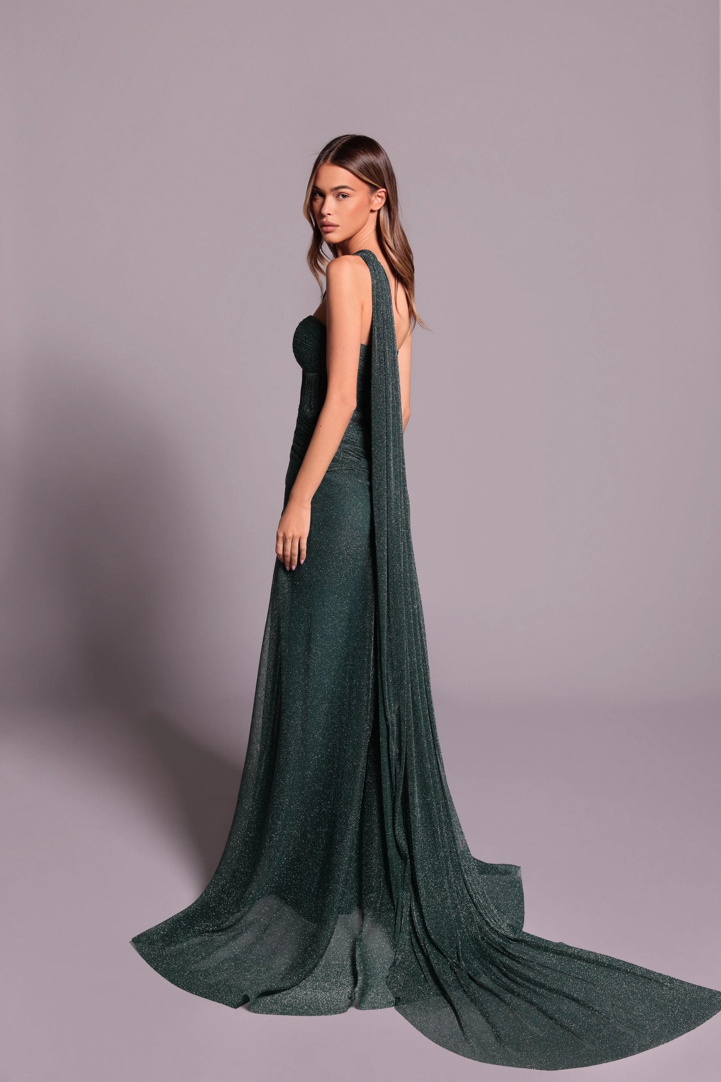 Woman wearing a dark green evening gown with a cape on a gray background