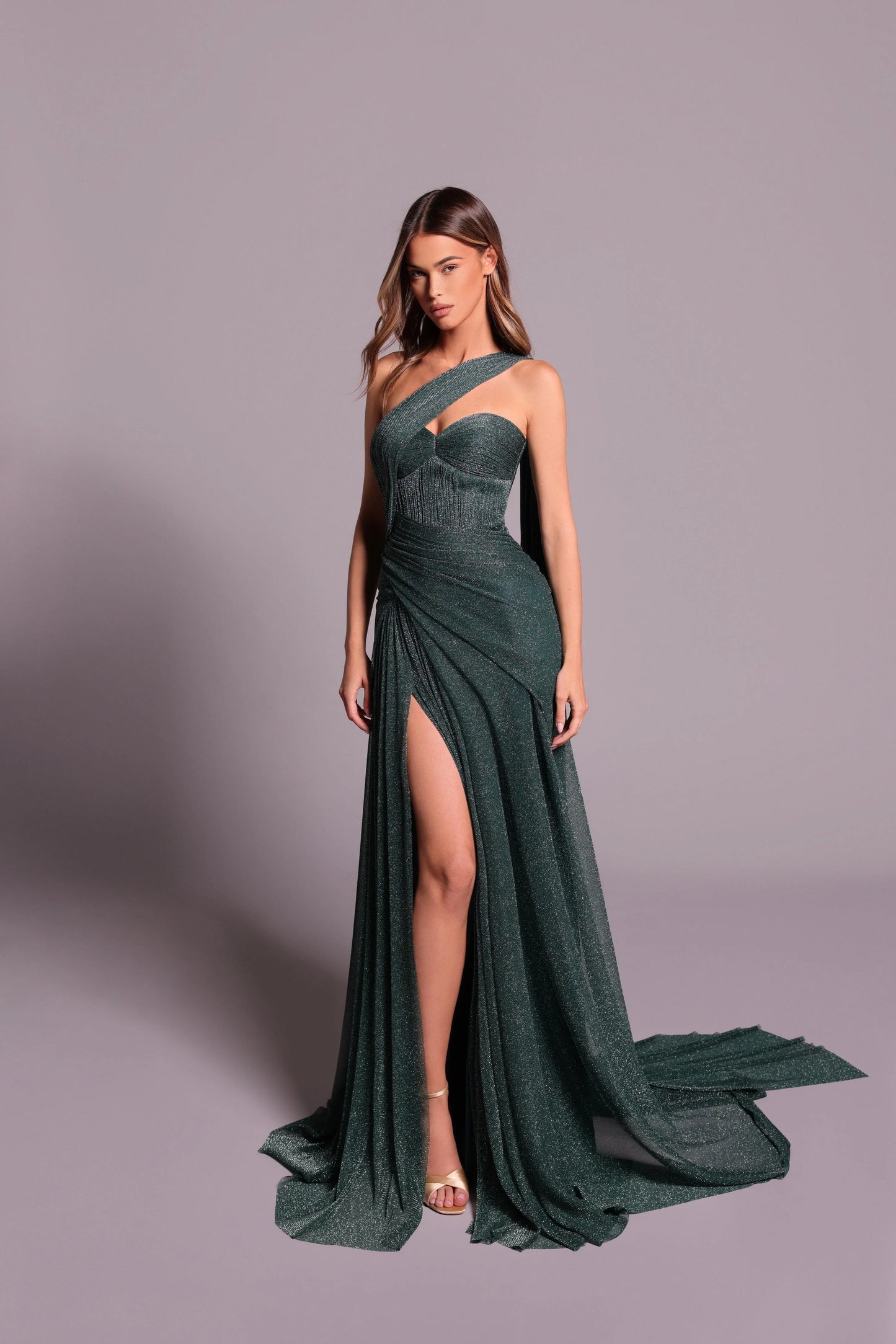 Woman wearing a green evening gown with a slit on a gray background