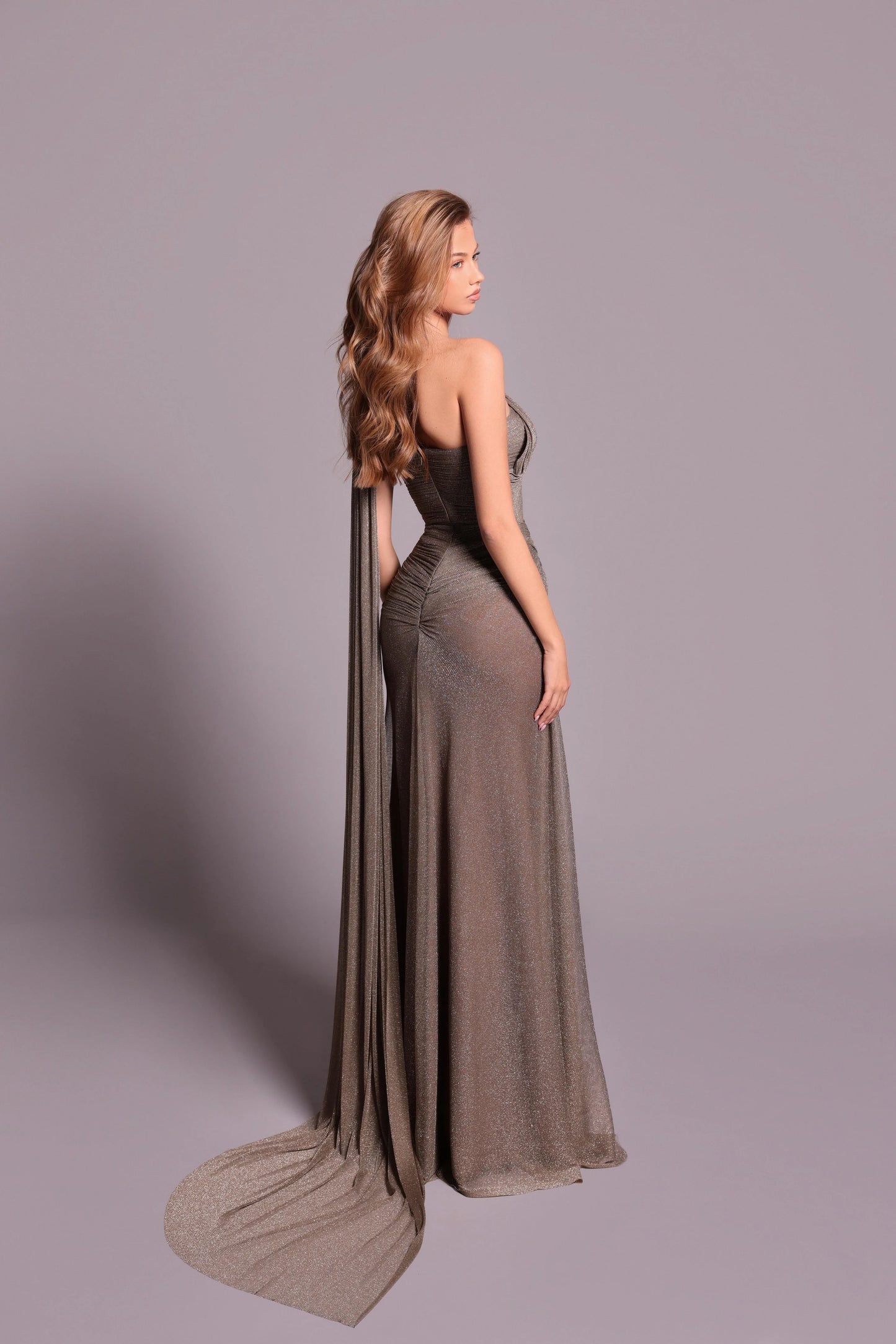 Model wearing Tarik Ediz 99041 Camellia gown featuring one-shoulder neckline, draped waist detail, thigh-high slit, and long train.