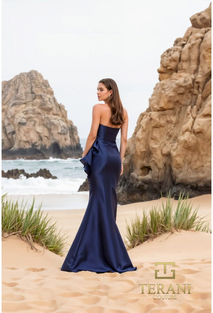 Model wearing Terani Couture 252E5550 strapless gown with peplum detail and mermaid silhouette on the beach. Model is wearing the dress in the color Navy. Back View.