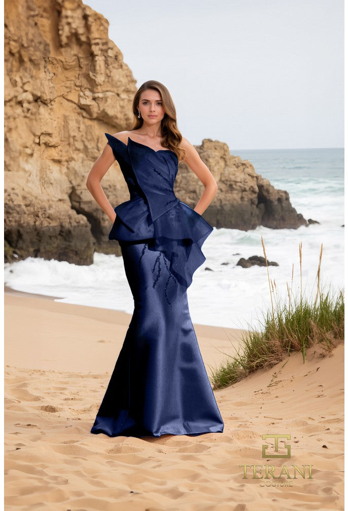 Model wearing Terani Couture 252E5550 strapless gown with peplum detail and mermaid silhouette on the beach. Model is wearing the dress in the color Navy.