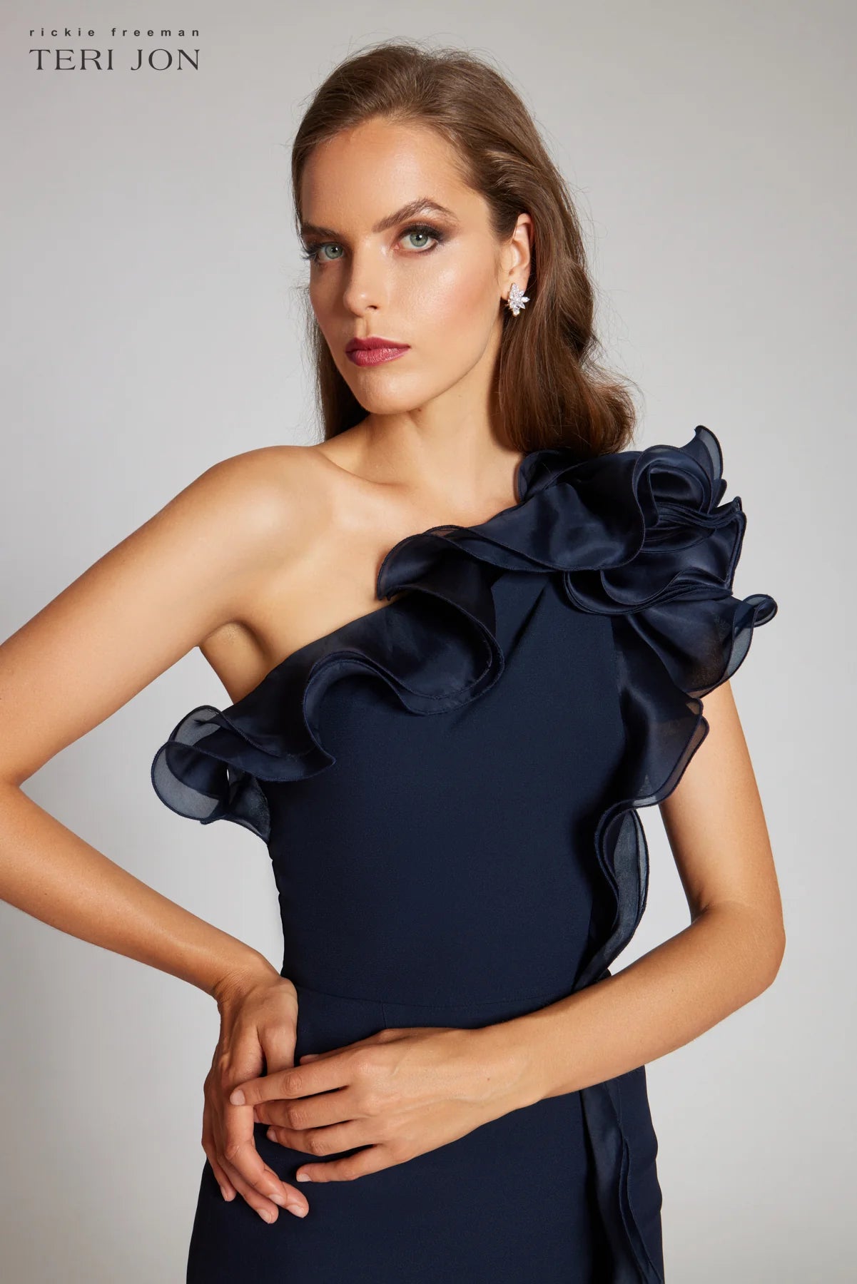 Teri Jon 249043 one-shoulder gown featuring a cascading ruffle detail and fitted silhouette. Perfect for formal evenings and mother of the bride or groom. Model is wearing the dress in the color navy. Close Up.