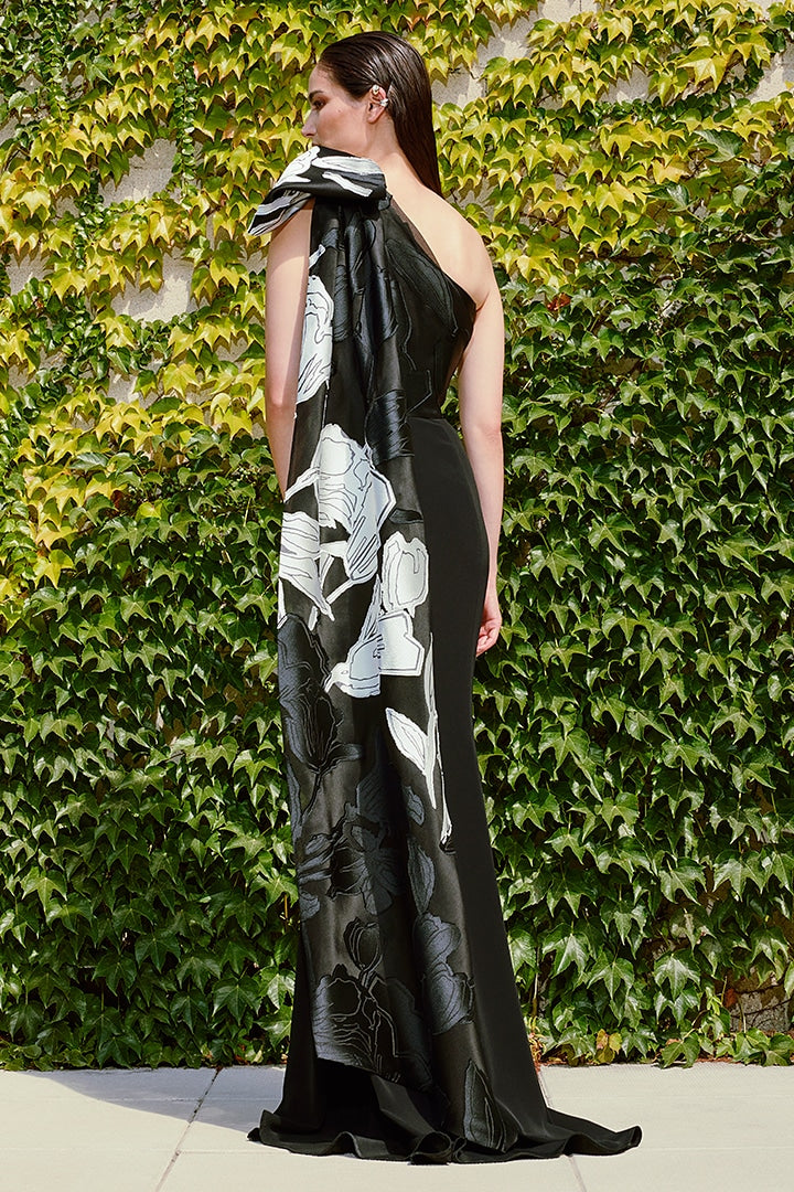 Woman wearing a black floral evening gown against a green ivy wall.