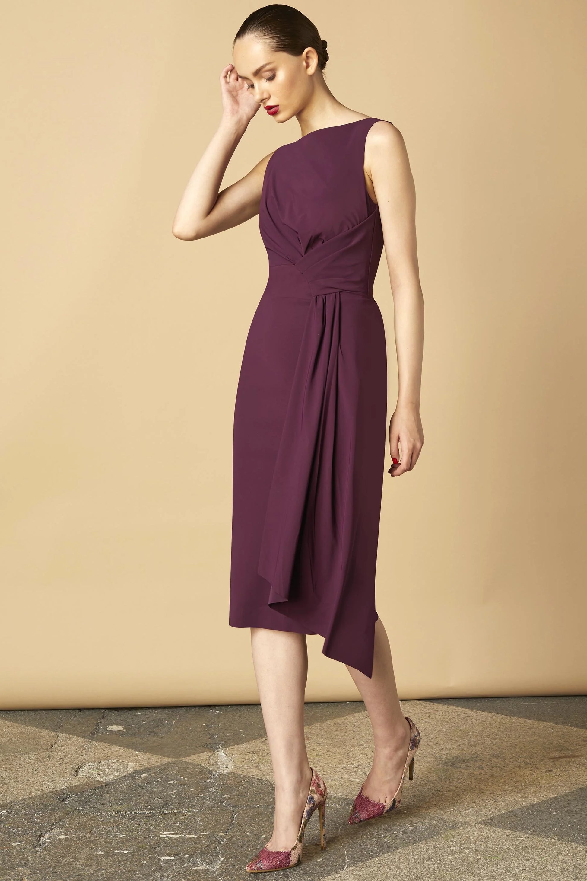 Model wearing Chiara Boni Cinthia draped asymmetric midi dress with bateau neckline and gathered waist detail.