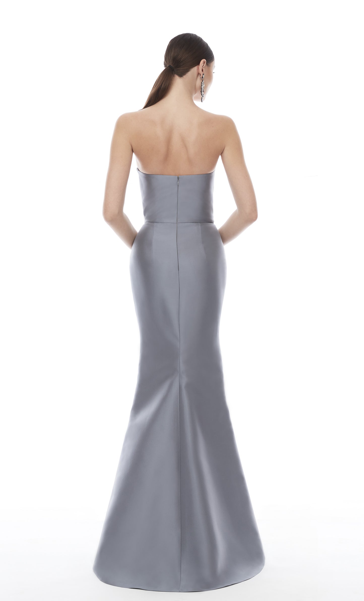 A woman shown from the back wearing a strapless fitted evening gown in a cool light gray or silver tone against a plain white studio background.