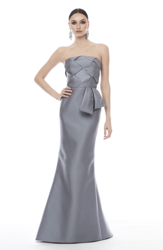 A woman modeling a strapless floor-length gown in a cool light gray or silver satin-like fabric. The dress has a structured, quilted-looking bodice with a large bow detail at the waist and a fitted mermaid silhouette.