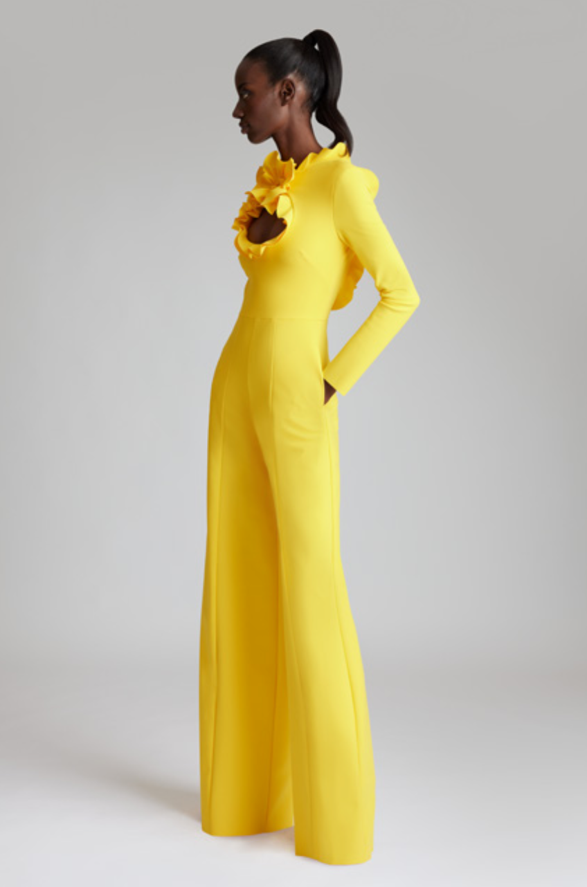 Woman wearing a bright yellow jumpsuit with floral details on a plain background