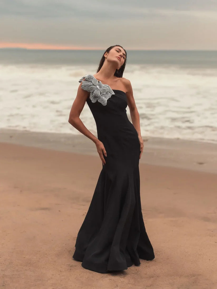 Model wearing Mac Duggal 11810 one-shoulder trumpet gown with flower detail, posing outdoors.