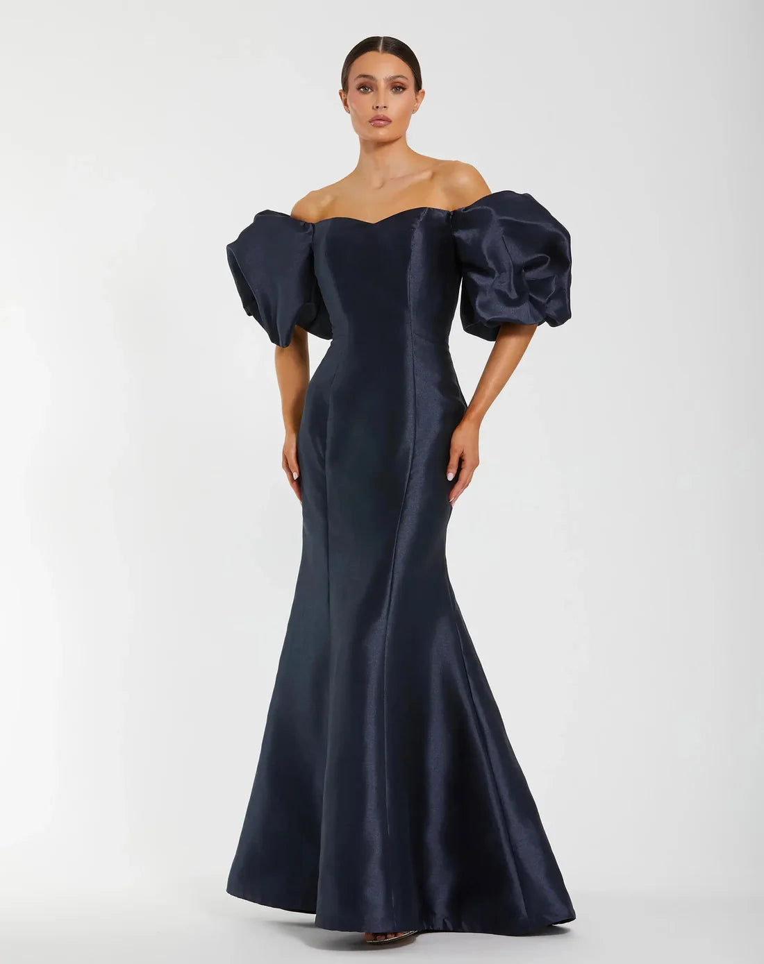 Model wearing Mac Duggal 50677 off-the-shoulder satin gown with puff sleeves, mermaid silhouette, and sweeping train.  Model is wearing the color midnight. Front view.