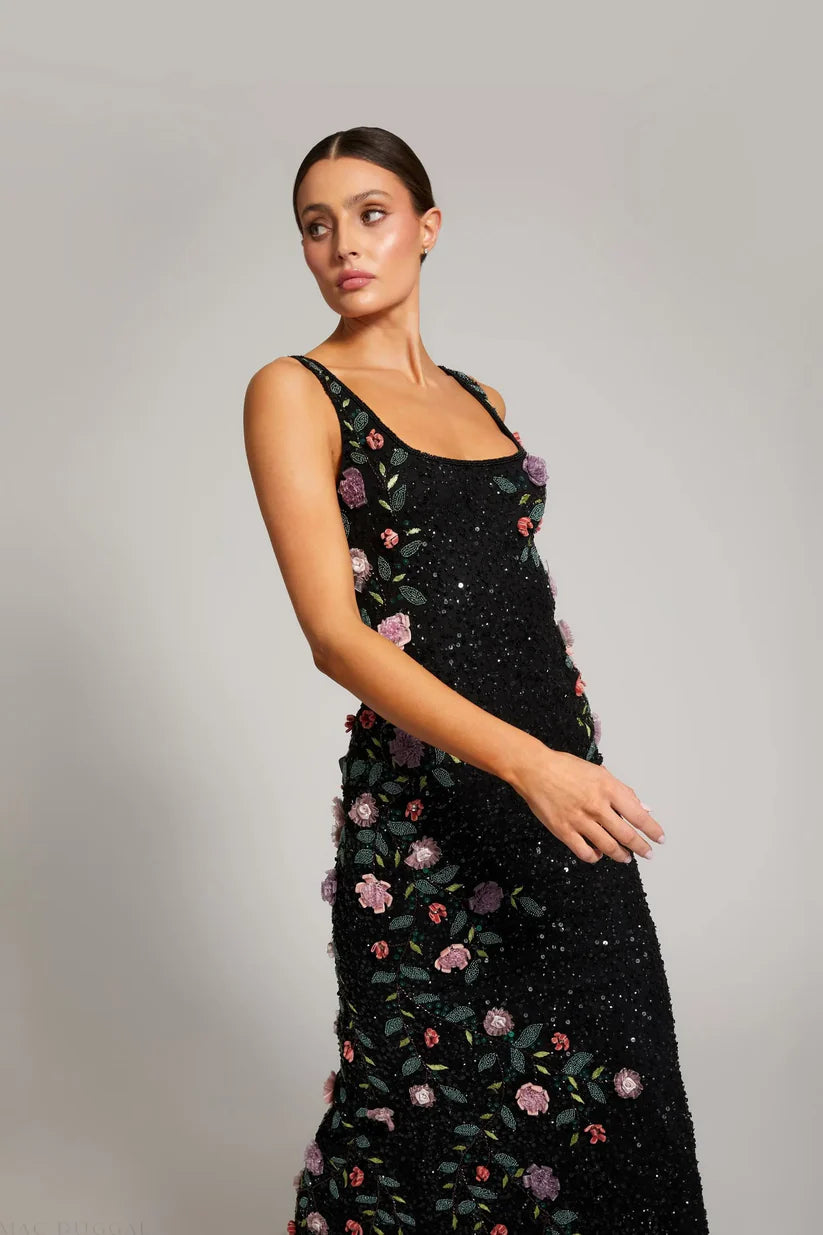 Woman wearing a black dress with floral embroidery on a gray background