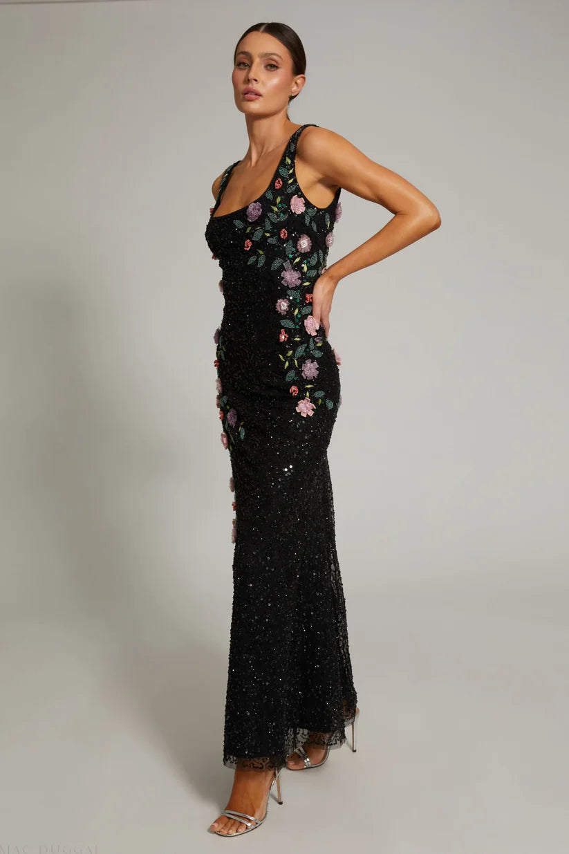 Woman wearing a black evening gown with floral embroidery on a plain background