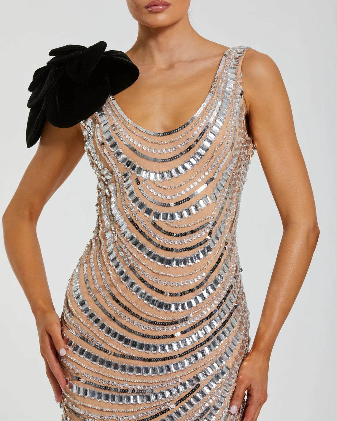 Model wearing Mac Duggal 94285 beaded gown with one-shoulder flower accent, cowl draped back, and ankle-length hem.