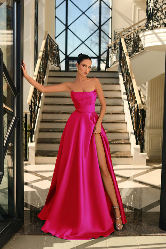 Model wearing Nicoletta NC1076 satin strapless gown with high slit in fushsia, showcasing ruched bodice and floor-length design.