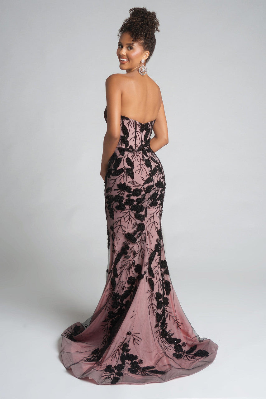 Woman wearing a pink evening gown with black floral lace details on a white background