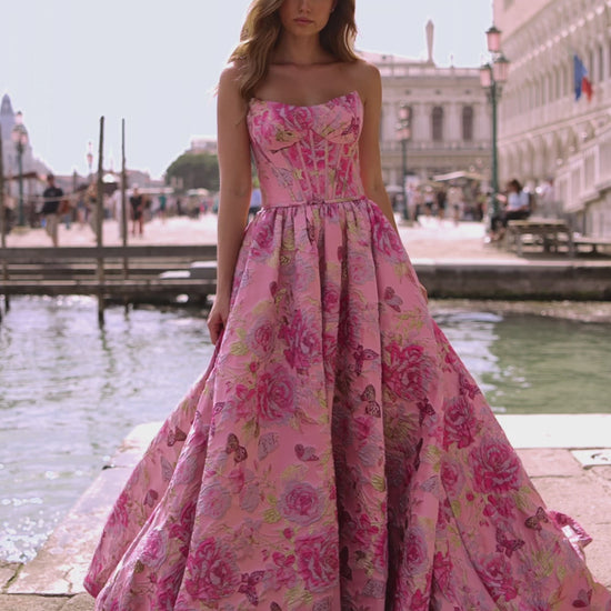 Model wearing Sherri Hill 57515 strapless ballgown with corset bodice and lace-up back, standing by a Venetian canal.  This is a video.