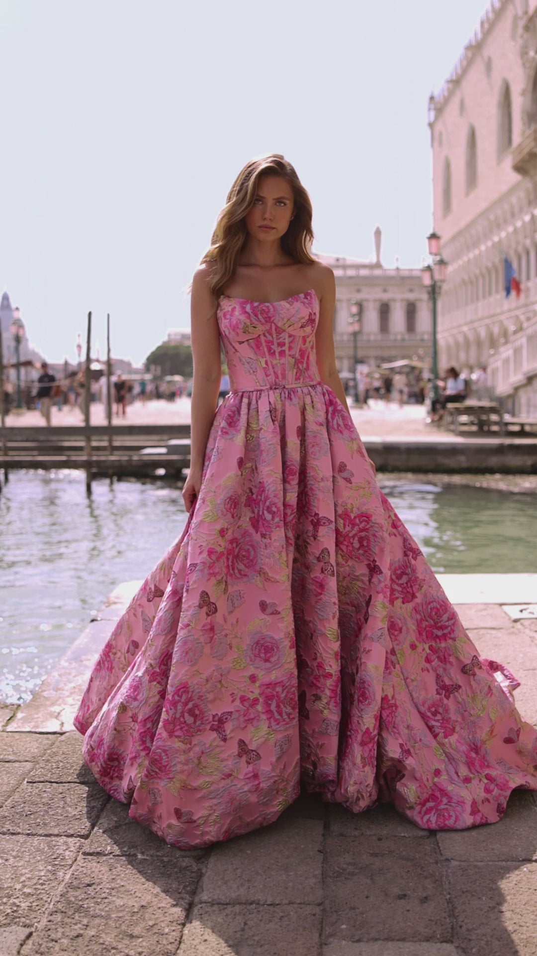 Model wearing Sherri Hill 57515 strapless ballgown with corset bodice and lace-up back, standing by a Venetian canal.  This is a video.