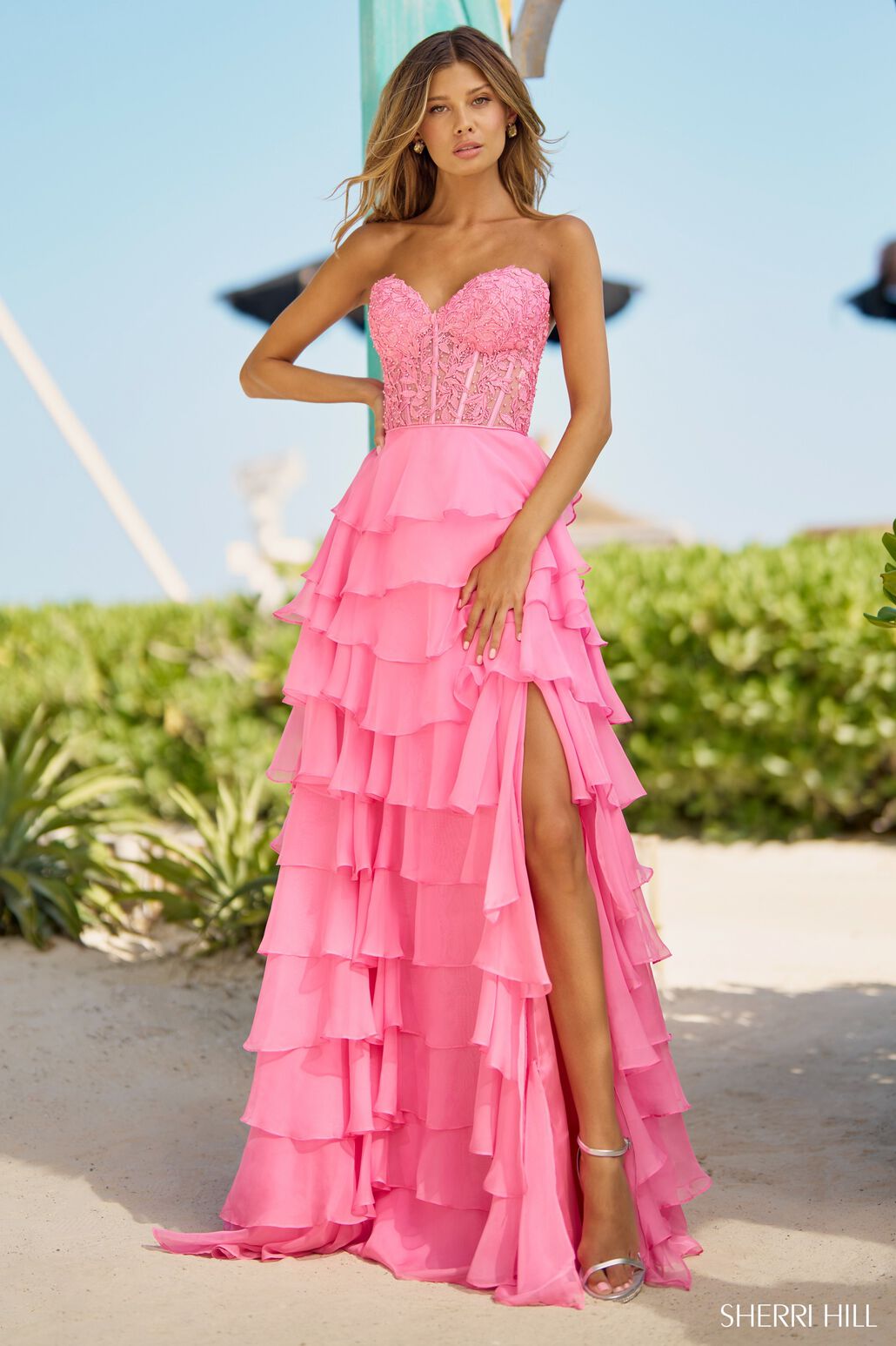 The Sherri Hill Strapless Leaf Lace Gown, a stunning ensemble featuring a leaf lace corset top, chiffon ruffle skirt with slit, and a lace-up back. Perfect for proms and formal events.