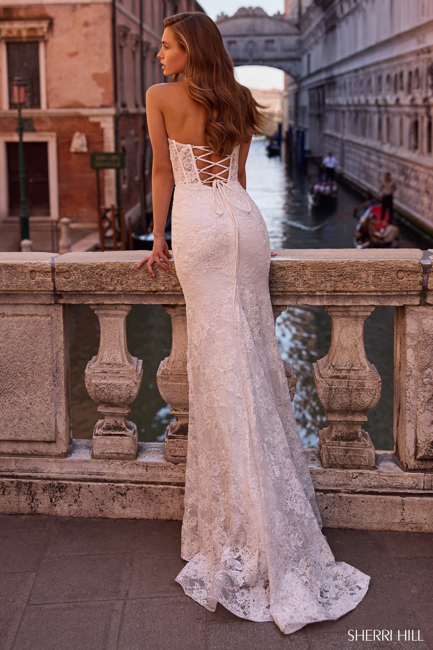 Model wearing the Sherri Hill 57448 strapless fitted gown with a corset bodice, shown from the front and back with elegant detailing.