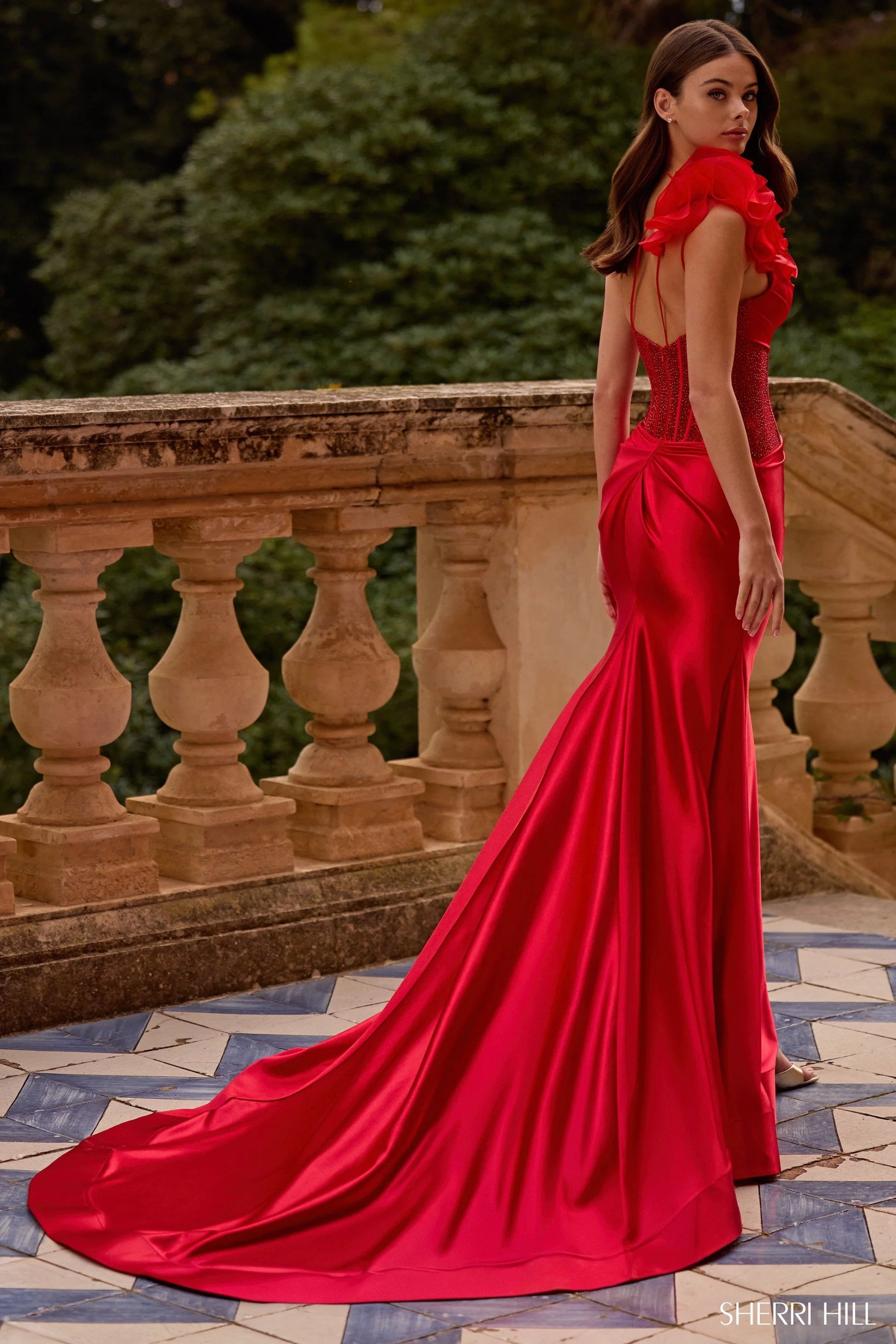 Model wearing Sherri Hill 57475 one-shoulder gown with rosette detail, corset bodice, and draped satin skirt with thigh-high slit.