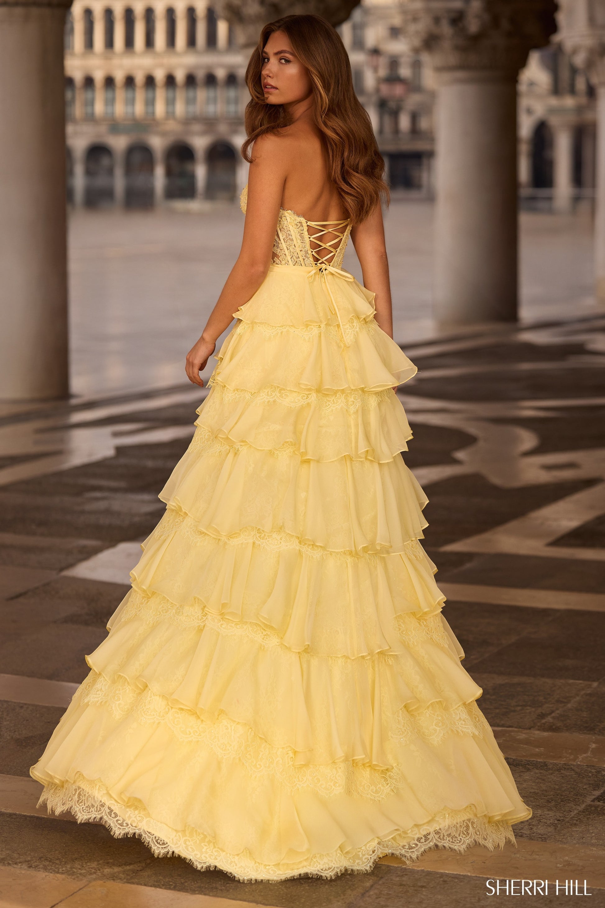 Woman in a yellow evening gown standing on a patterned floor with architectural background