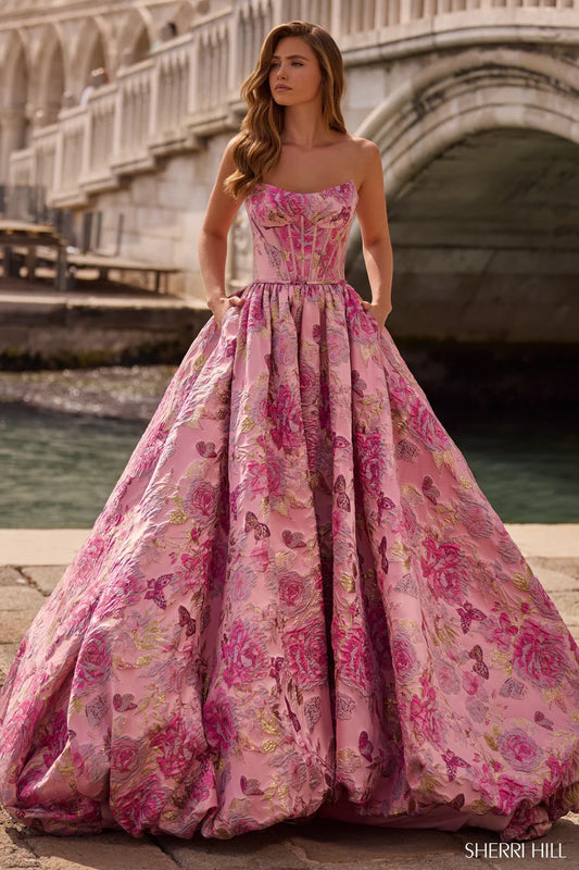 Woman in a pink floral gown standing by a bridge with water in the background