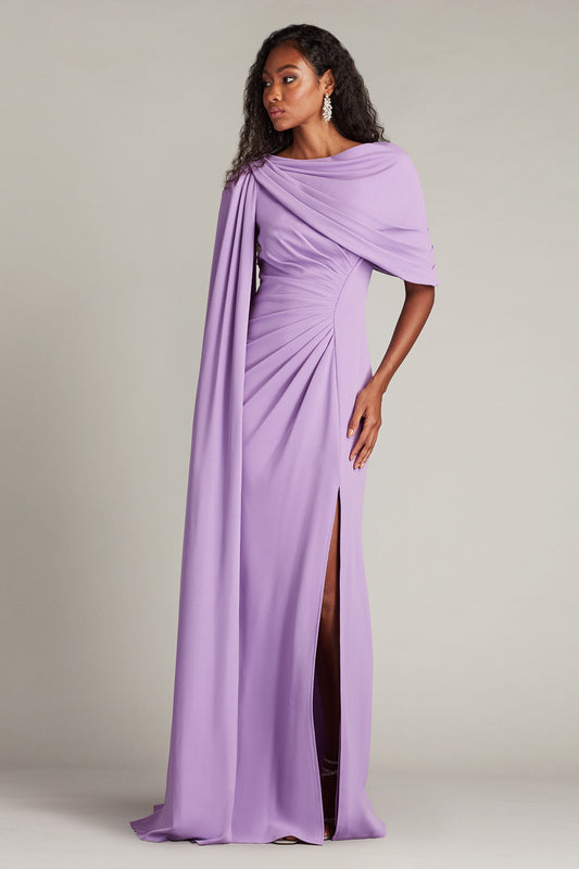 Model wearing Tadashi Shoji BOS25345L gown with one-shoulder cape, pleated bodice, and side slit, shown in front and back views.