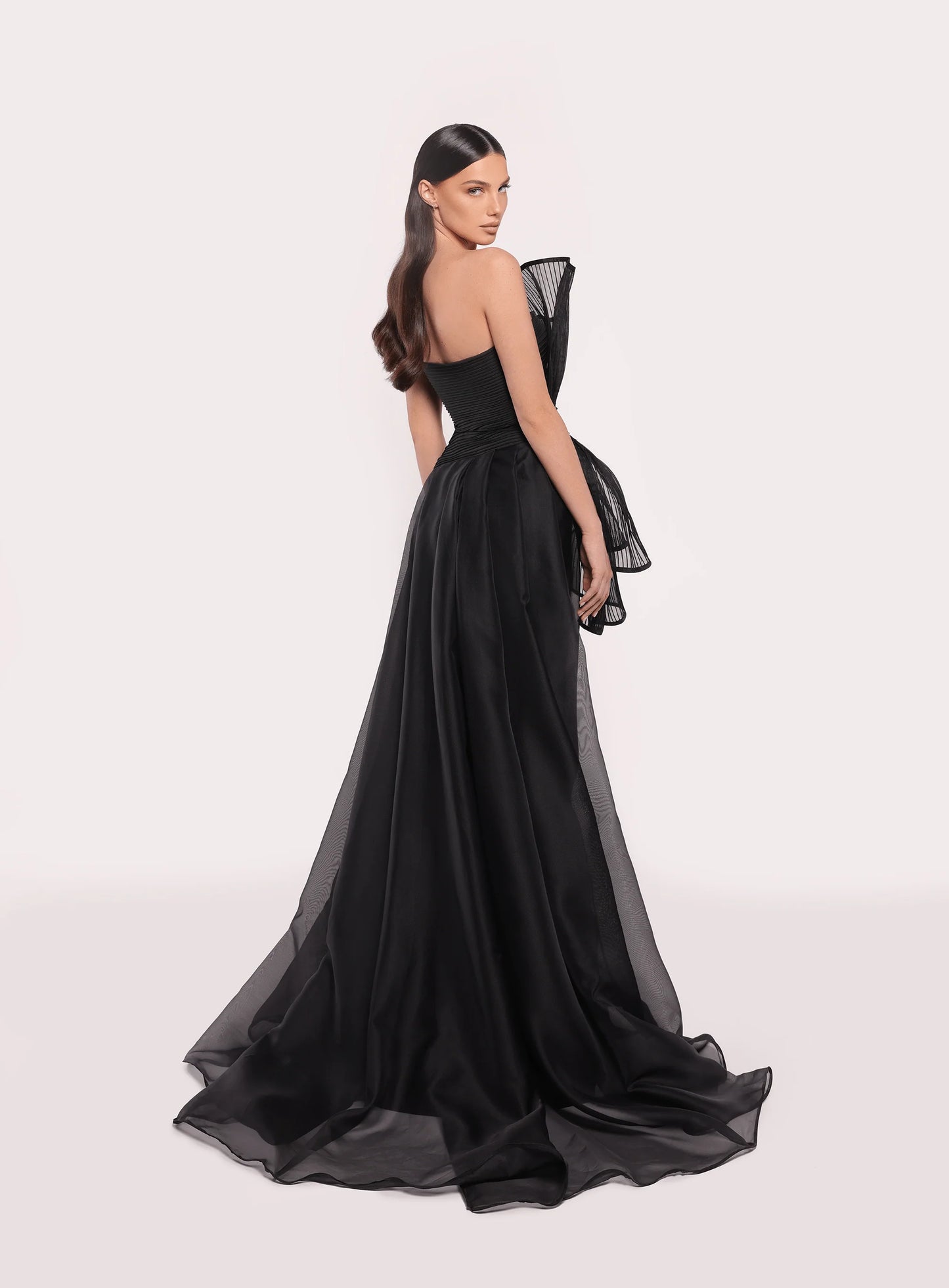 Model wearing Tarik Ediz 98708 Ronesme strapless gown in the color black with sculptural pleated bodice and full A-line skirt with train, ideal for red carpet or formal events.