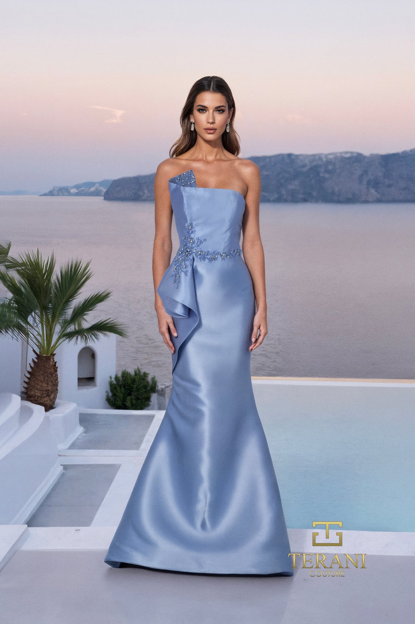 Woman in a light blue evening gown standing in front of a scenic backdrop with palm trees and a pool.